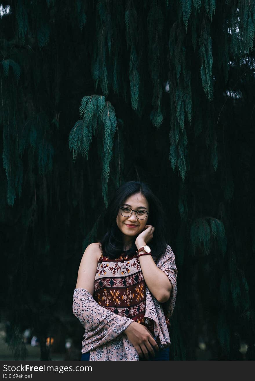 Woman in Brown Floral Top Stands Beside Tree