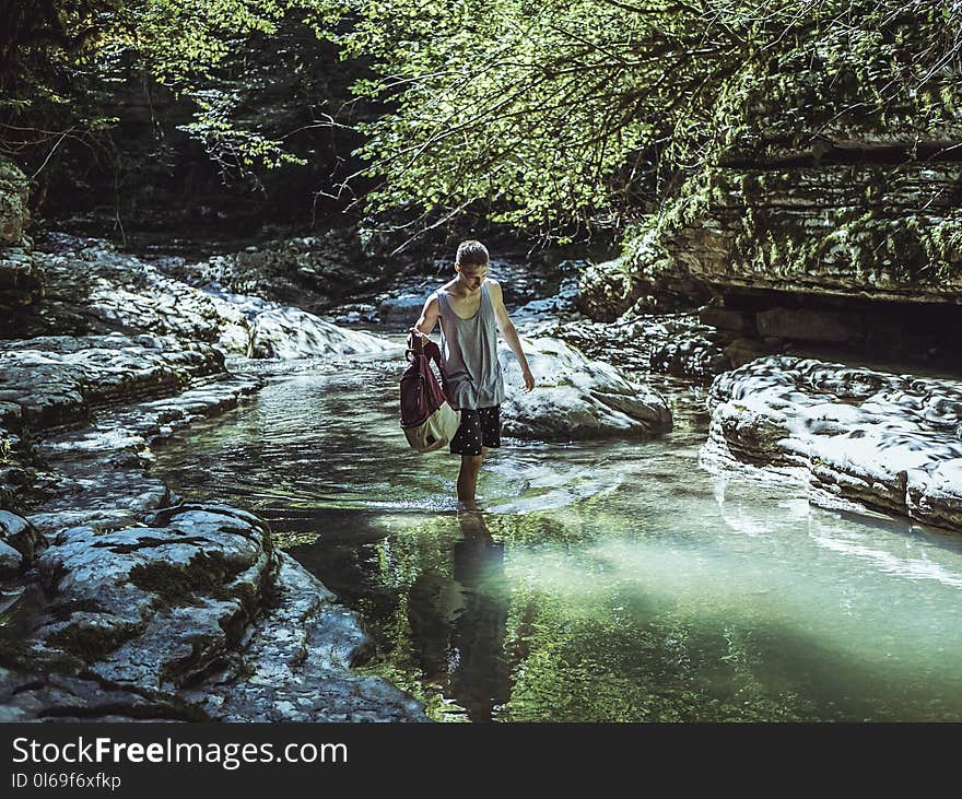 Man Walking on River in Between Stone and Tree