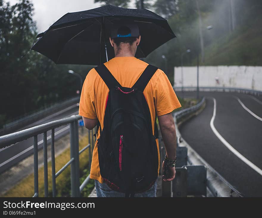 Man Wearing Orange Shirt Holding Black Umbrella