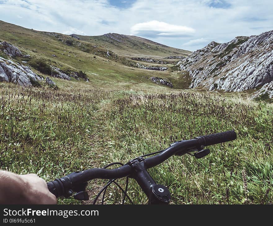 Person Riding Bicycle Overlooking Green Grass Field and Hill