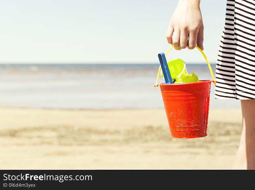 Woman holding bucket with children`s beach toys - spade and shovel on a sunny day.