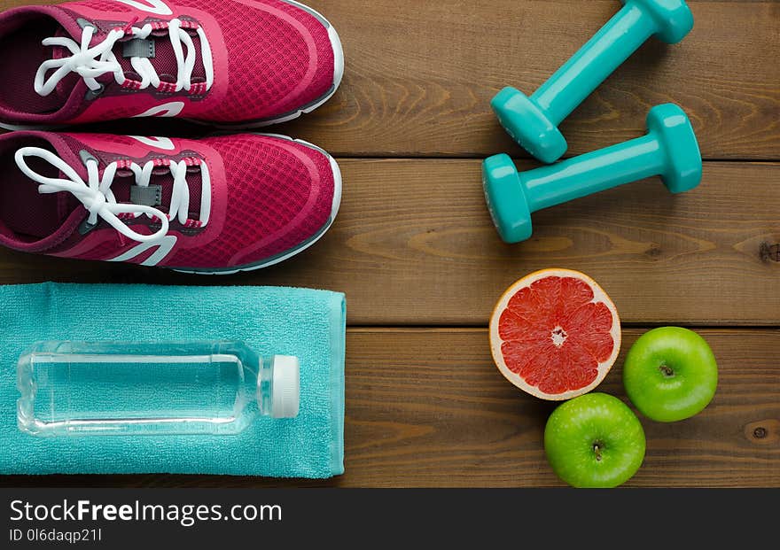 Fitness concept with sneakers dumbbells bottle of water apple pomelo and measure tape on wooden table background