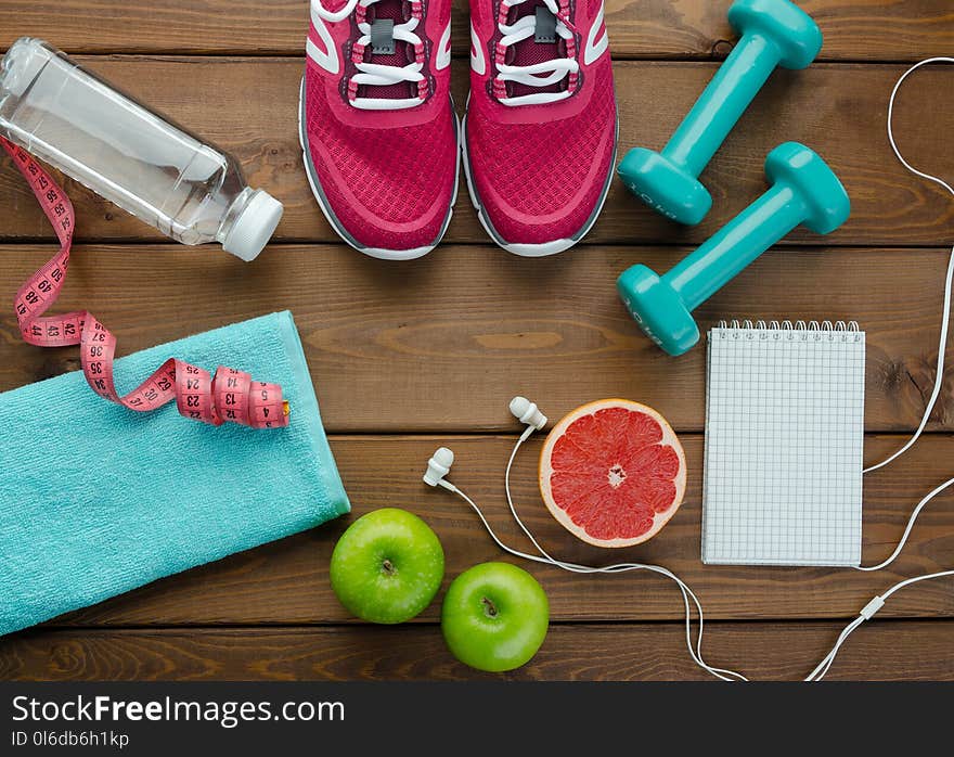 Fitness concept with sneakers dumbbells bottle of water apple pomelo and measure tape on wooden table background