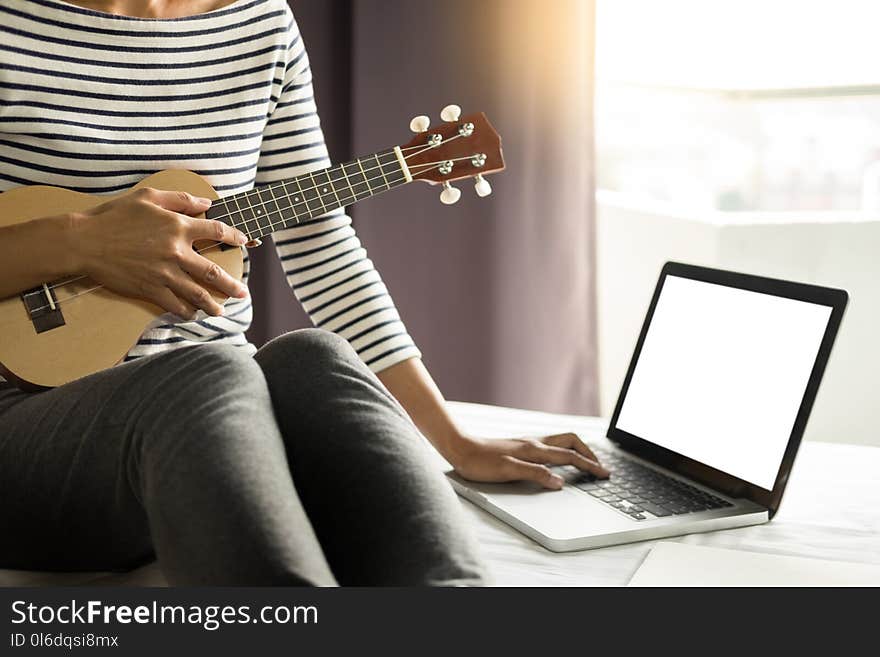 Happy young asian woman playing ukulele sitting on bed in bedroom.