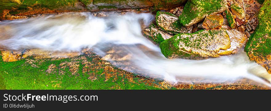 Water cascade of small creek between mossy stones. Long exposure.