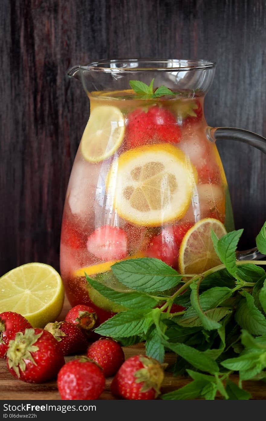 Lemonade with strawberry, lemon, mint, lime and ice cubes in a glass jug surrounded by the ingredients