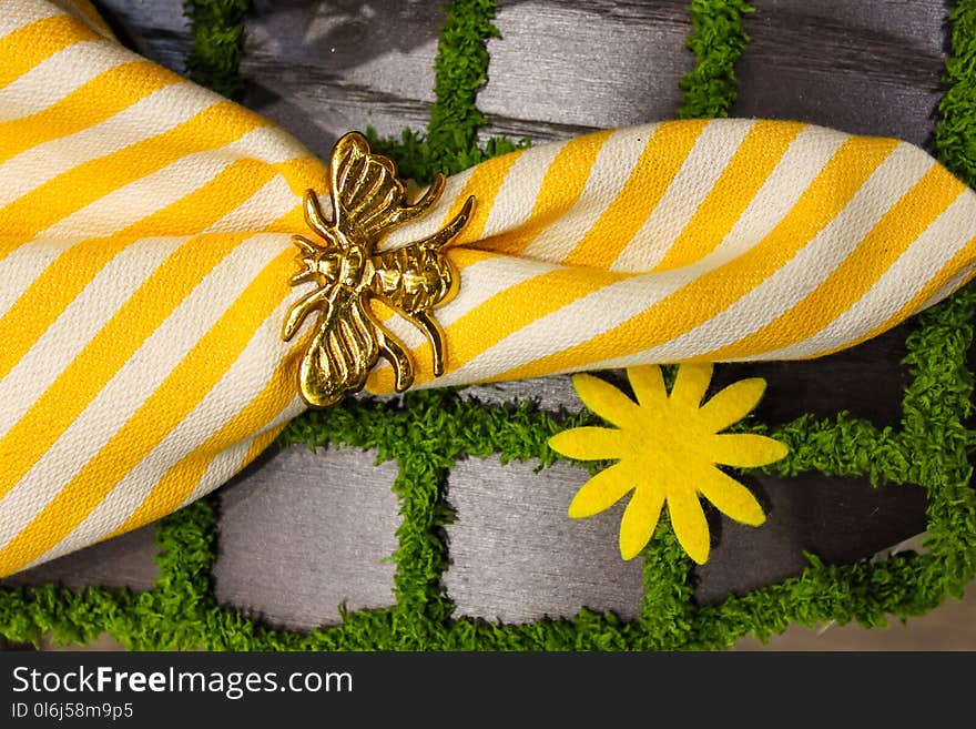 A Yellow and white crisp linen napkin with gold bee napkin ring on a placemat that looks like paving stones with grass- springtime theme