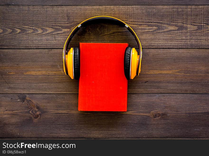 Audiobooks concept. Headphones put over hardback book with empty cover on dark wooden background top view copy space