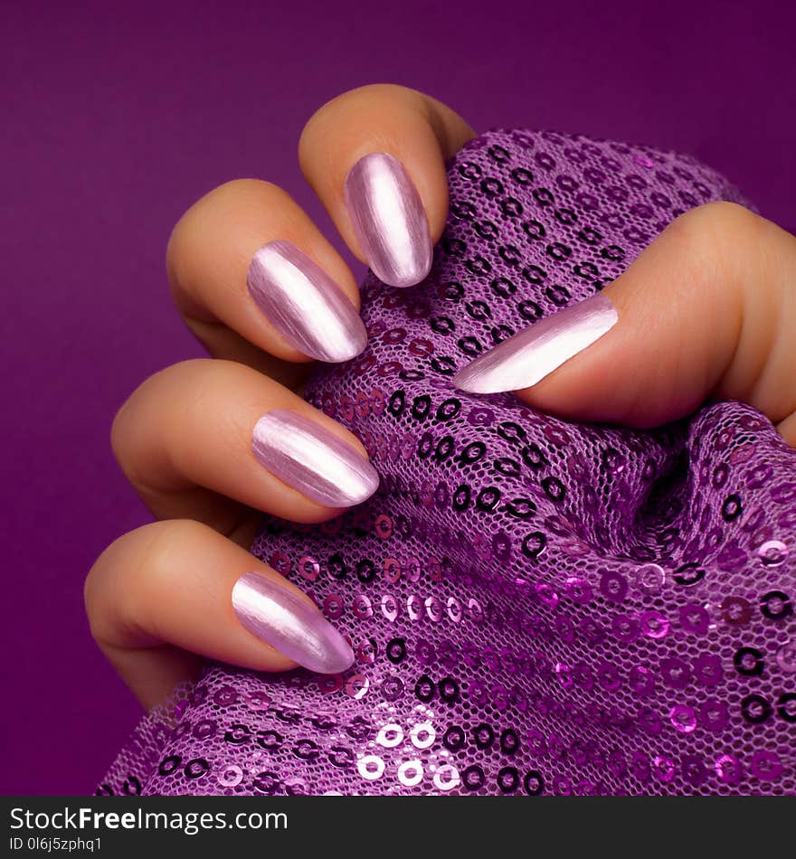 Female hand with shiny bright purple nails is holding glittered purple textile on purple background, nail care and manicure concept. Female hand with shiny bright purple nails is holding glittered purple textile on purple background, nail care and manicure concept.