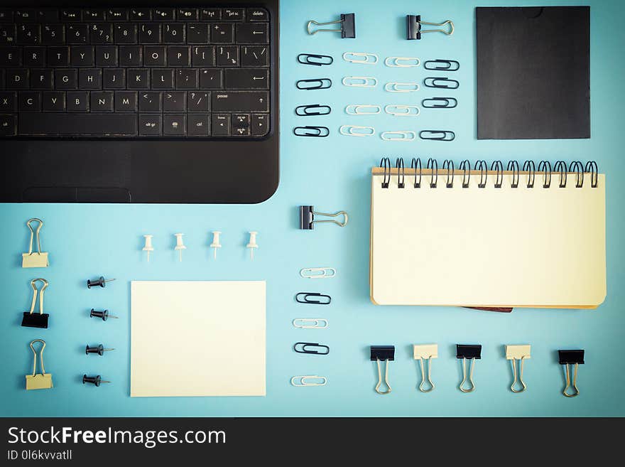 On a blue background there is an open notepad on the springs. Staples, buttons and paper clips are neatly arranged in rows. Beautiful pattern, mock up. Photo with a vignette.