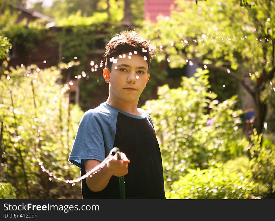 Kid hands hold hose with squirting water on the summer sunny green garden