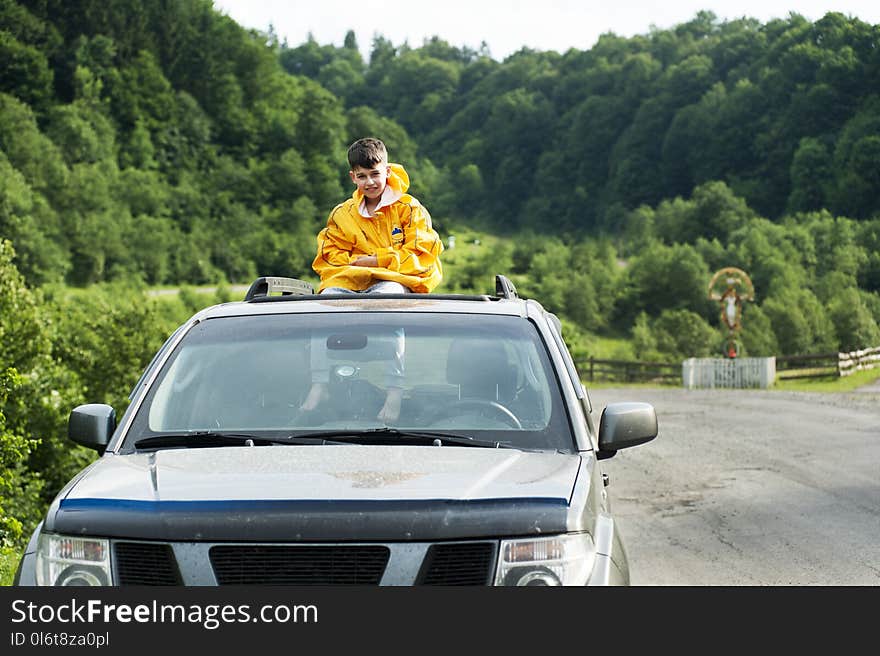 Child in Yellow Jacket Sitting on Roof of Nissan Frontier Through the Sunroof