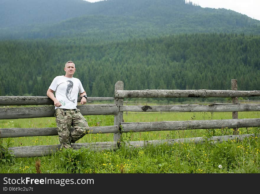 Photo of Man Leaning on Wooden Fence