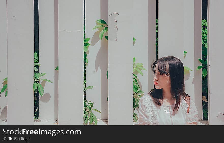 Woman Wearing White Shirt Leaning on White Wooden Fence With Plants