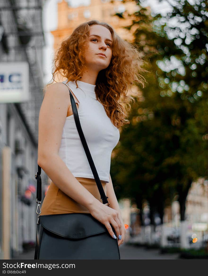 Woman in White Turtleneck Sleeveless Top and Brown Bottoms Holding Black Leather Crossbody Bag Outfit