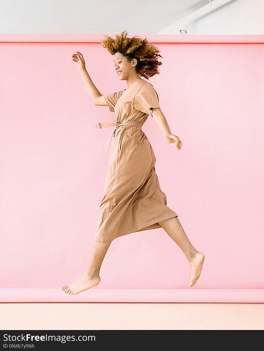 Woman Wearing Brown Dress Jump Near Pink Wall