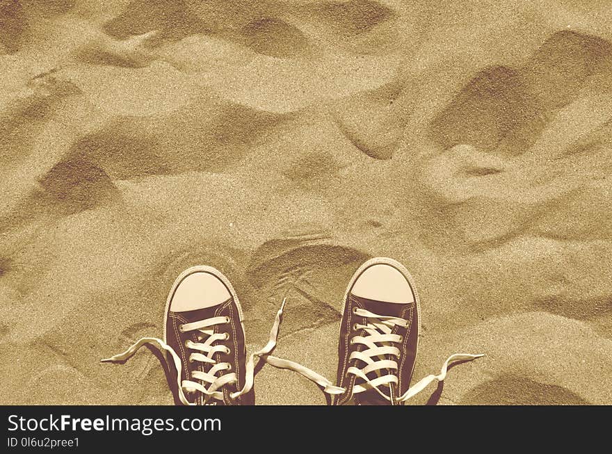 Looking down on pair of blue unlaced sneakers standing side by side on beach sand. Hot sunny weather. Summer vacation. Retro styled photo. Copy space. Looking down on pair of blue unlaced sneakers standing side by side on beach sand. Hot sunny weather. Summer vacation. Retro styled photo. Copy space