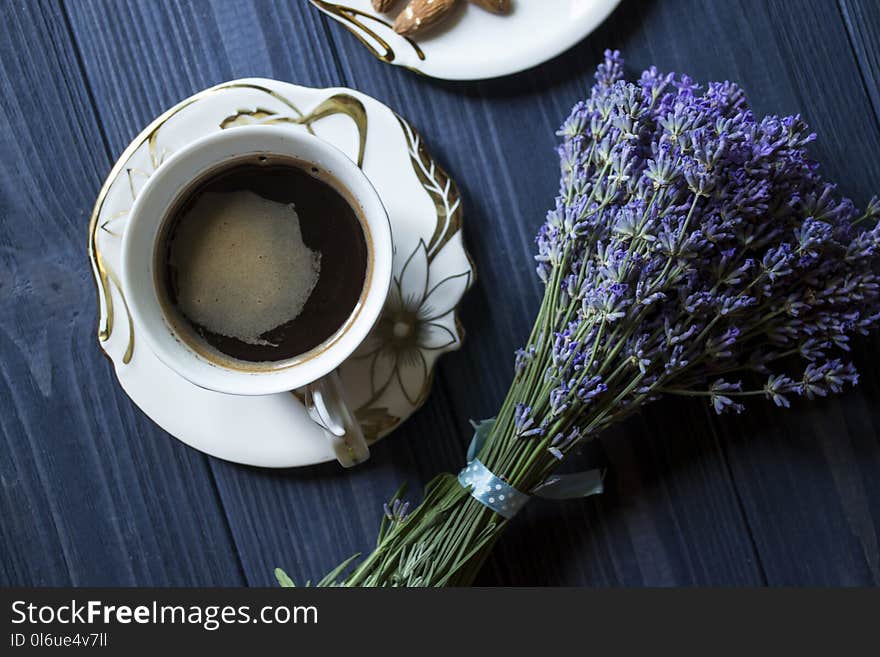 A cup of coffee and bouquet of lavender on a dark blue wooden table.