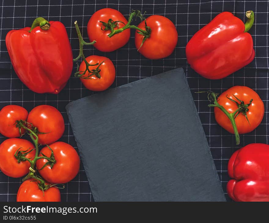 Red tomatoes on a branch, red pepper, cutting board slate on black cloth background with blank space for text. Flat lay. Top view