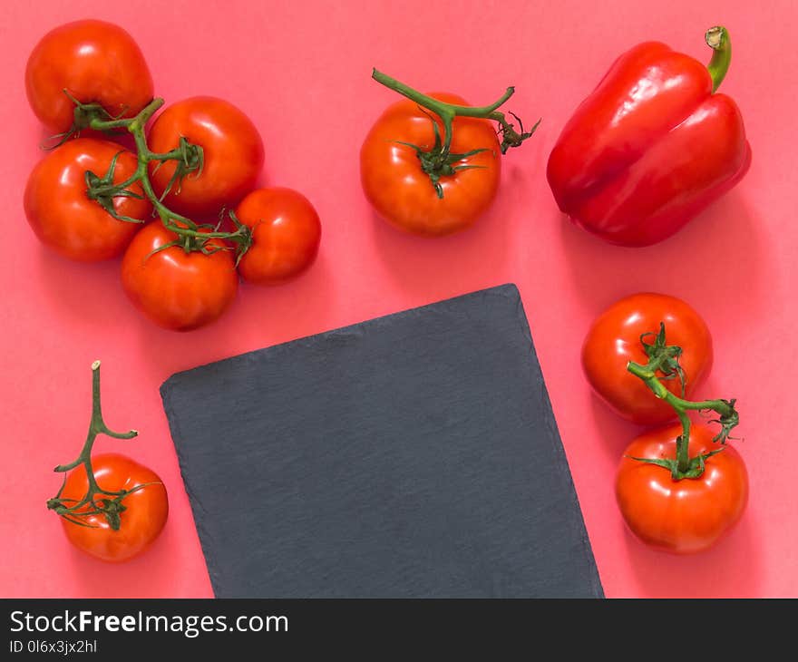 Red tomatoes on a branch, cutting board slate on a pink background with blank space for text. Flat lay. Top view. Copy space.