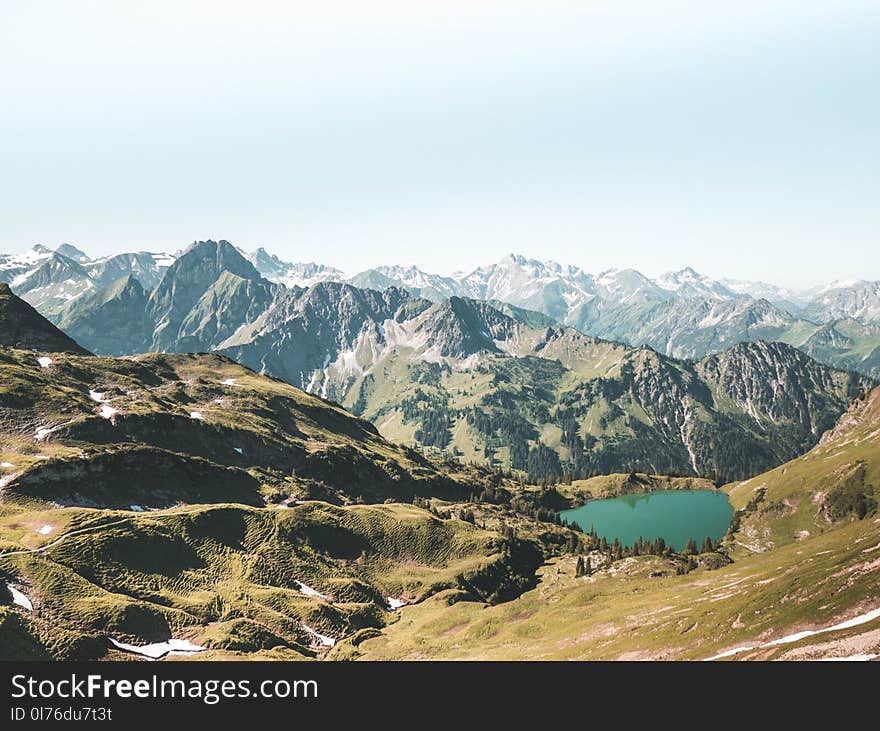 Beige and Green Mountain With Teal Lake Under White Sky at Daytime