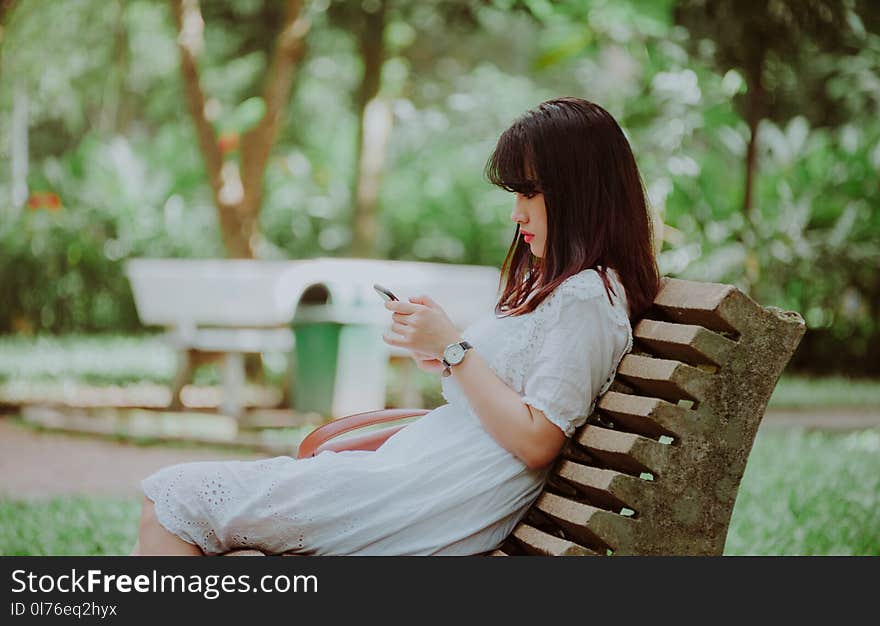 Woman Sitting on Bench Checking Her Phone