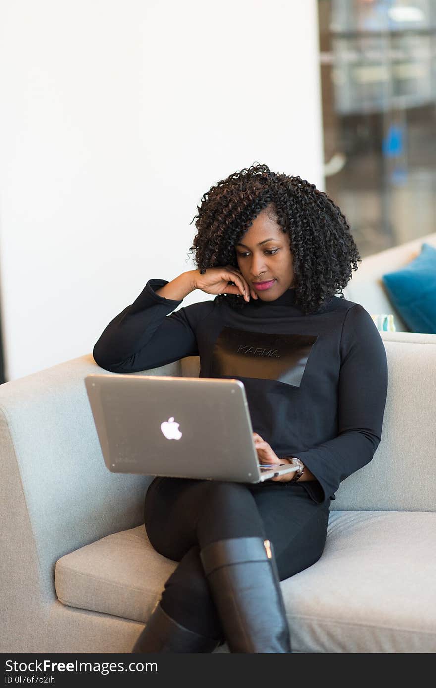 Woman in black outfit with MacBook sitting on a couch.