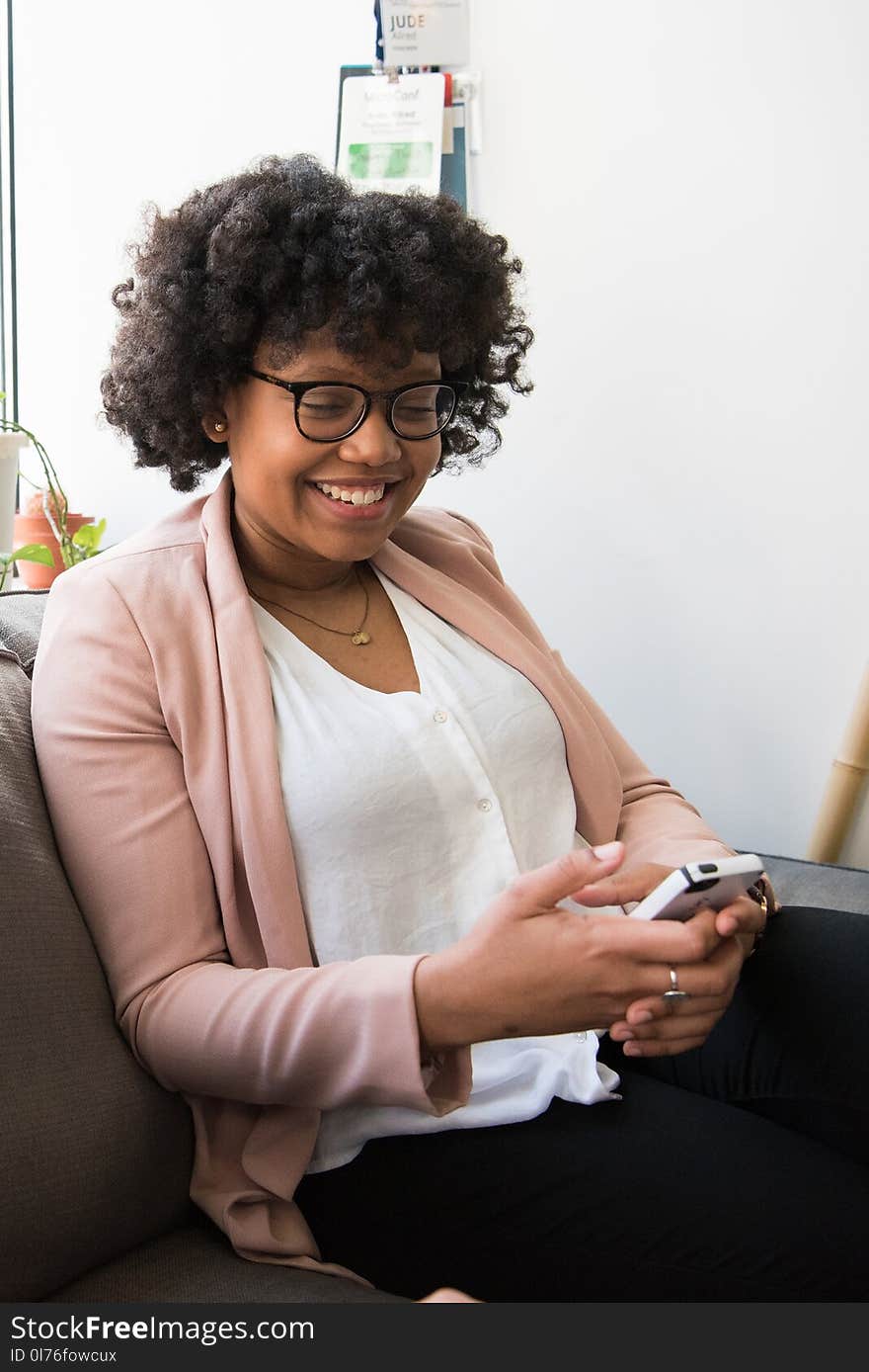 Smiling Woman Wearing White Top and Pink Cardigan Holding Iphone Sitting on Couch