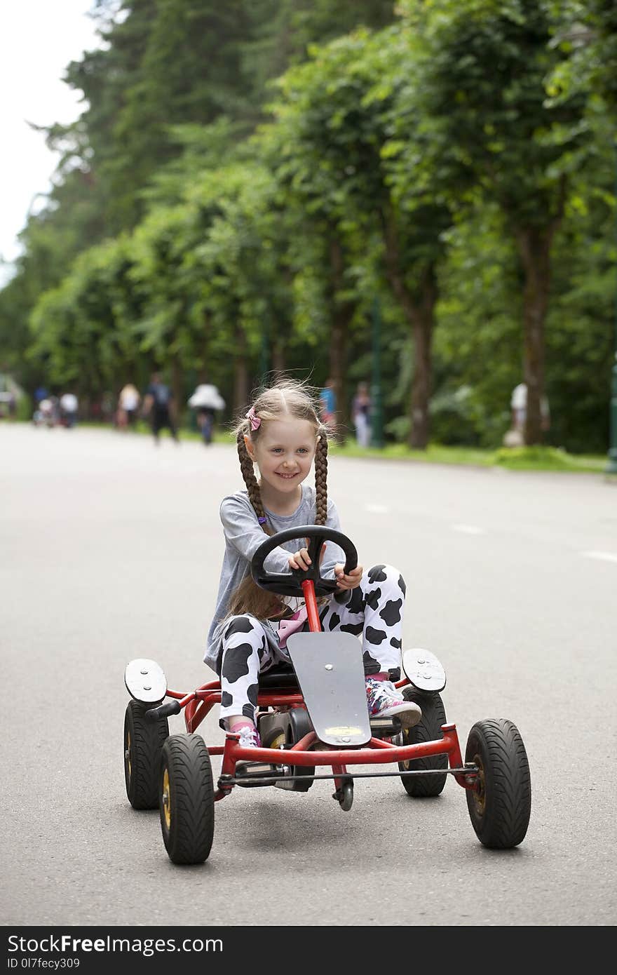 Little girl with two tails driving kids racing carand smiling. Little girl with two tails driving kids racing carand smiling