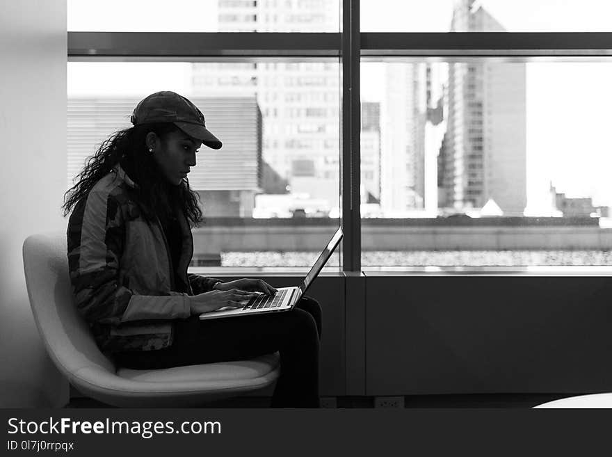 Grayscale Photo Of Woman Wearing Cap And Jacket Using Laptop