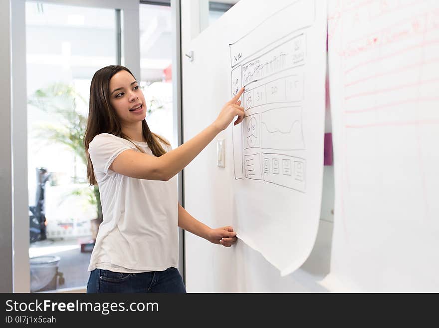 Woman Wearing White Shirt Standing Beside White Board While Pointing on White Paper