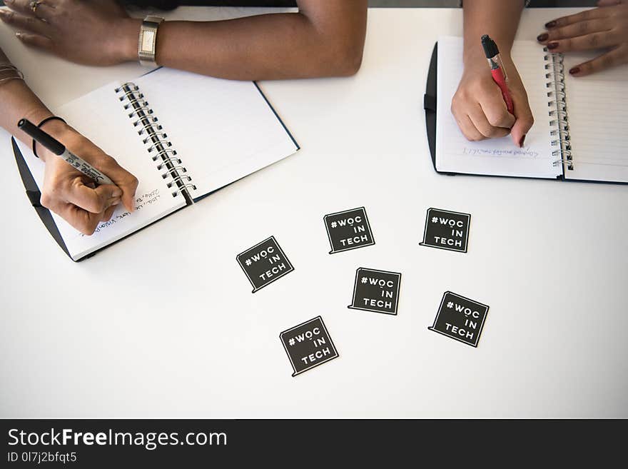 Two Peoples Holding Black and Red Pens Writing on White Ruled Note