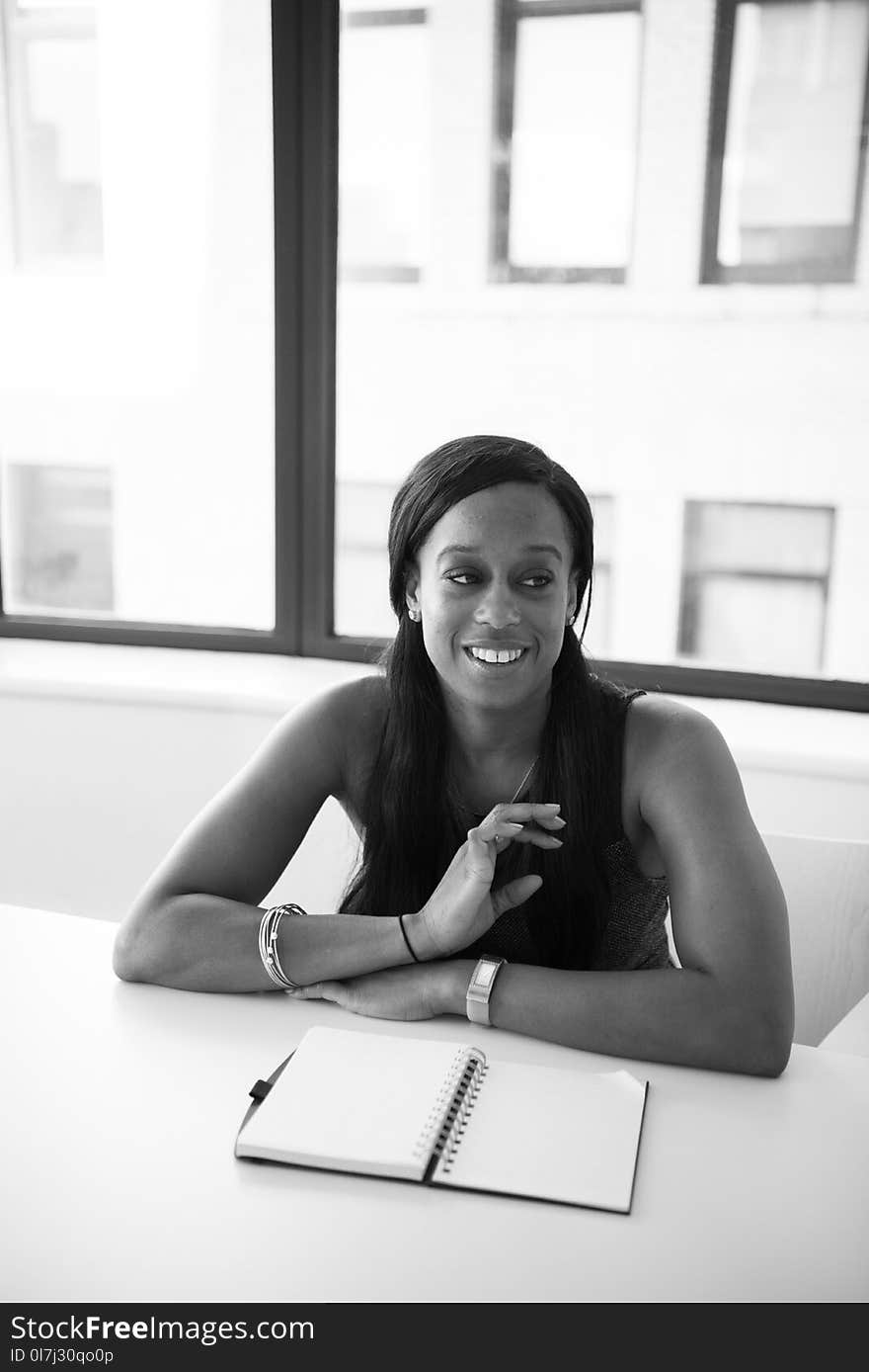 Grayscale Photography of Woman in Sleeveless Top Sits Near Table