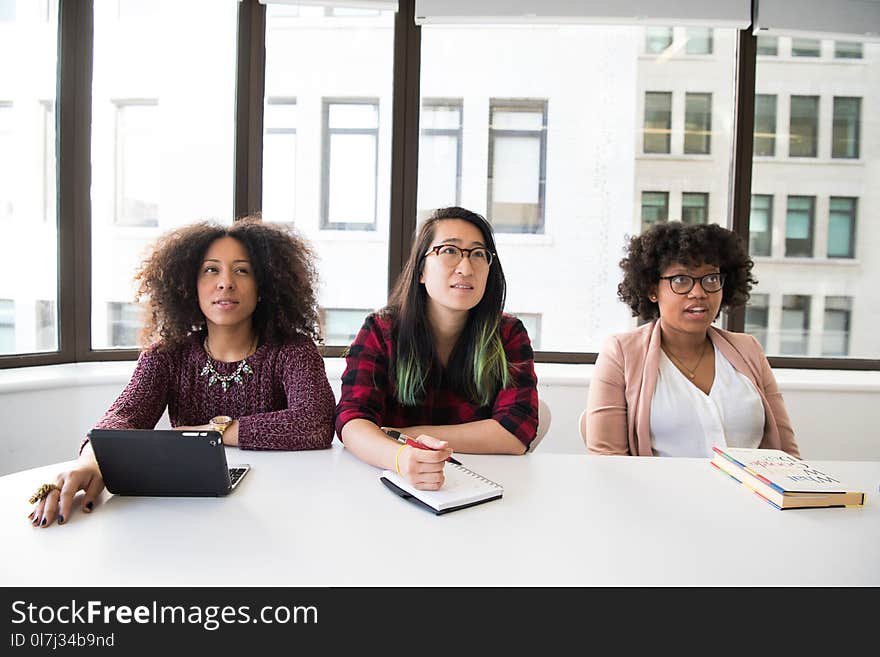 Closeup Photo of Three Women Sit on Chair in Front of Tables