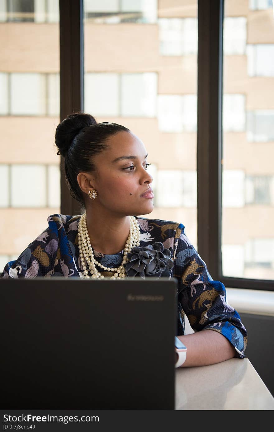 Woman Wearing Blue and Brown Floral Elbow-sleeved Dress Facing Black Lenovo Laptop Near Glass Window