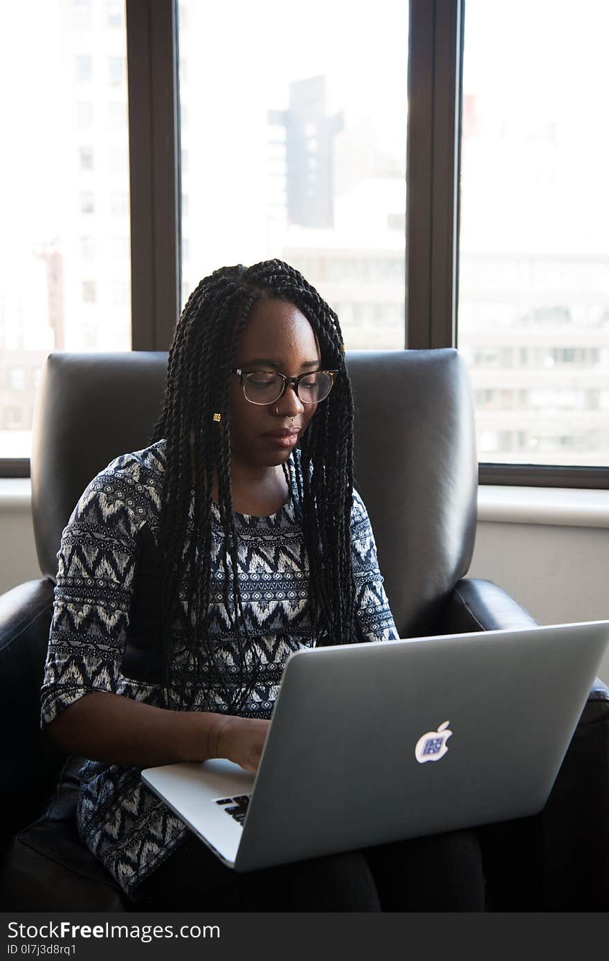 Woman in Black and White Blouse Sitting on Black Leather Chair Holding Her Laptop