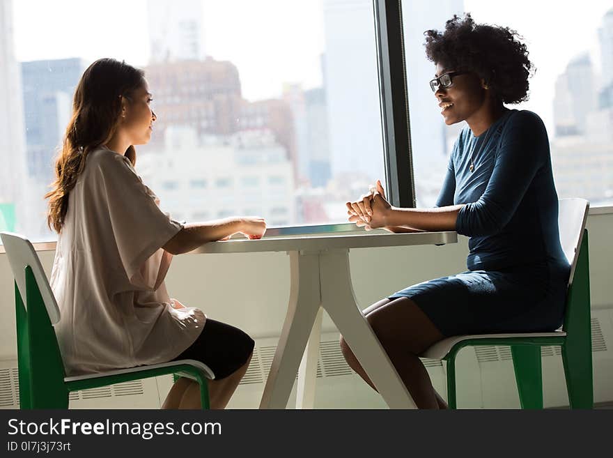 Two Women Sitting on Chairs Beside Window