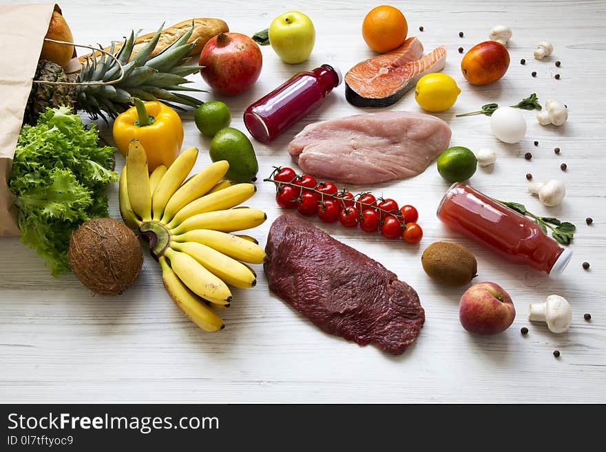 Full paper bag of various healthy food over white wooden background, side view.