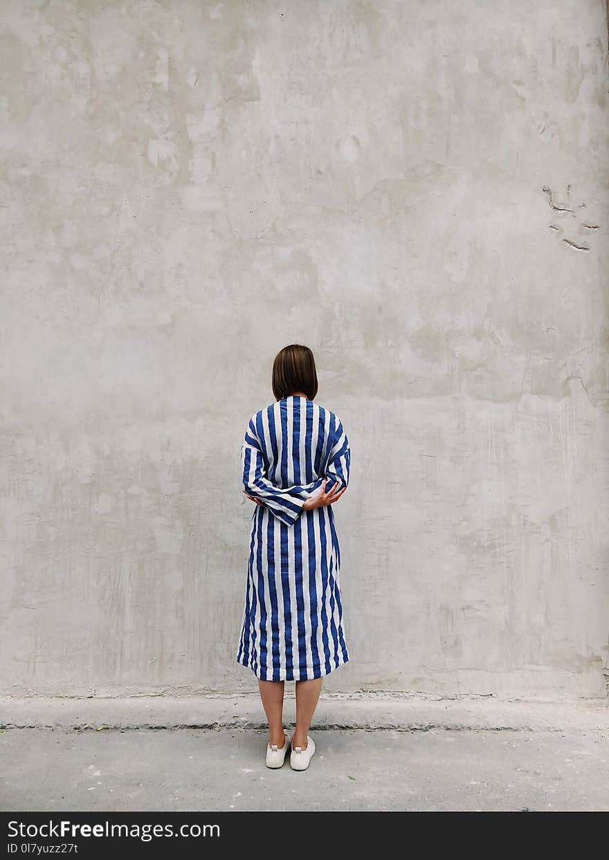 Woman Wearing Blue and White Striped Shirt Dress Facing Gray Wall