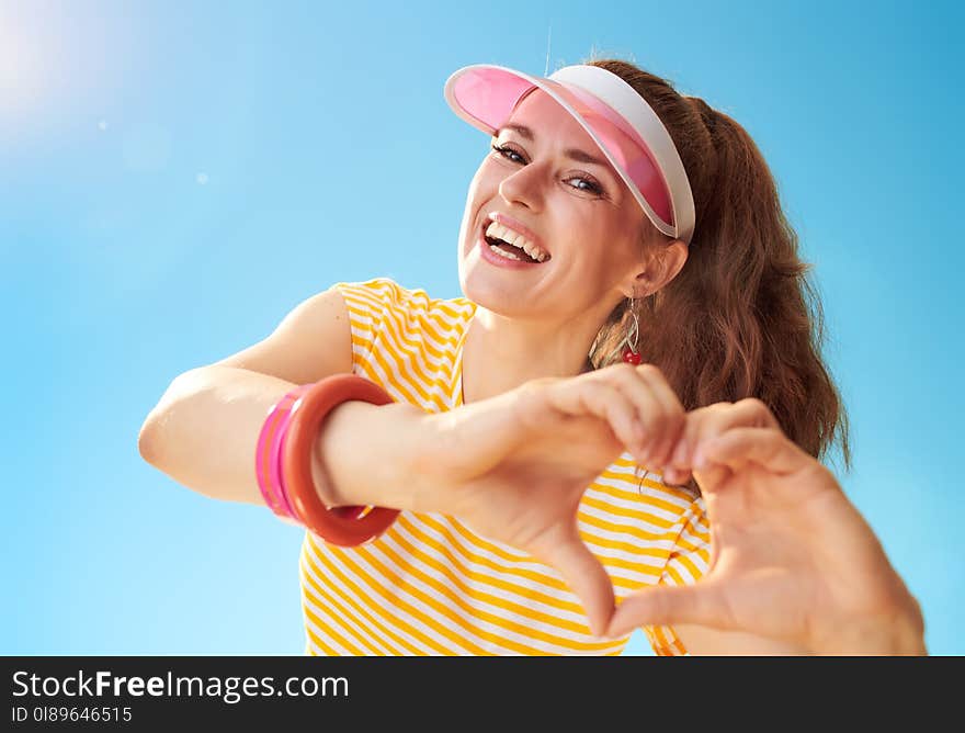 Happy young woman against blue sky showing heart shaped hands