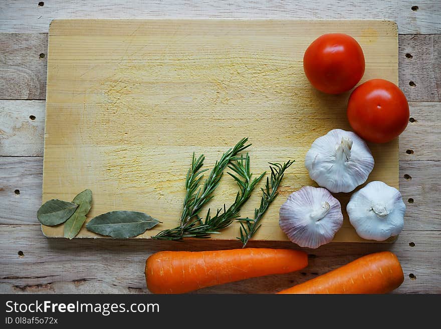 Many fresh ingredients, rosemary, spaghetti, carrot, tomato, garlic, onion and bay leaf on chopping board with wooden table background, copy space, cooking concept