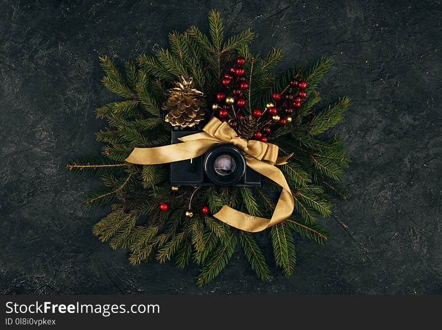 top view of photo camera and festive decorations on fir branches on dark tabletop