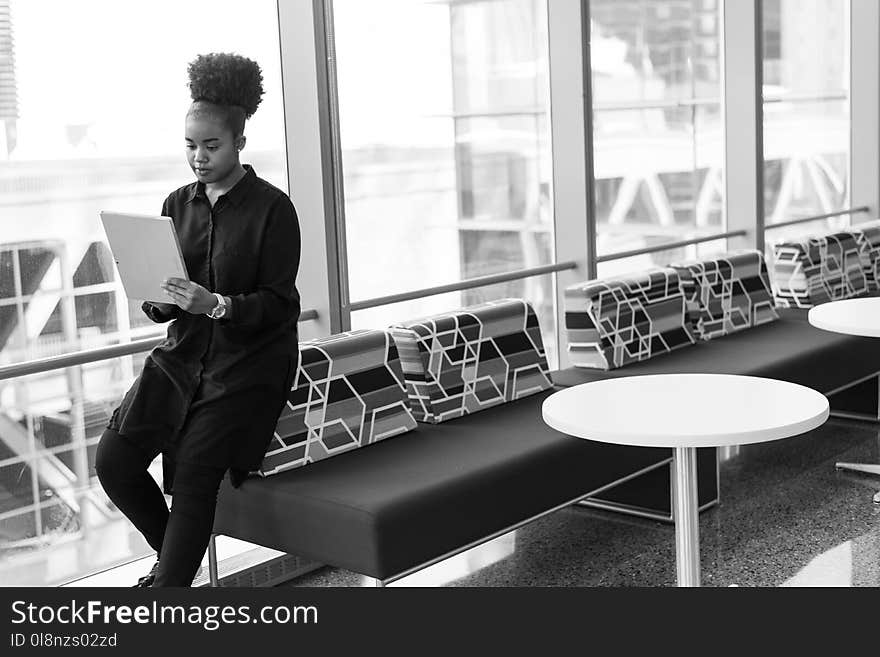 Grayscale Photo of Woman Holding Gray Notebook on Sofa Near Glass Window