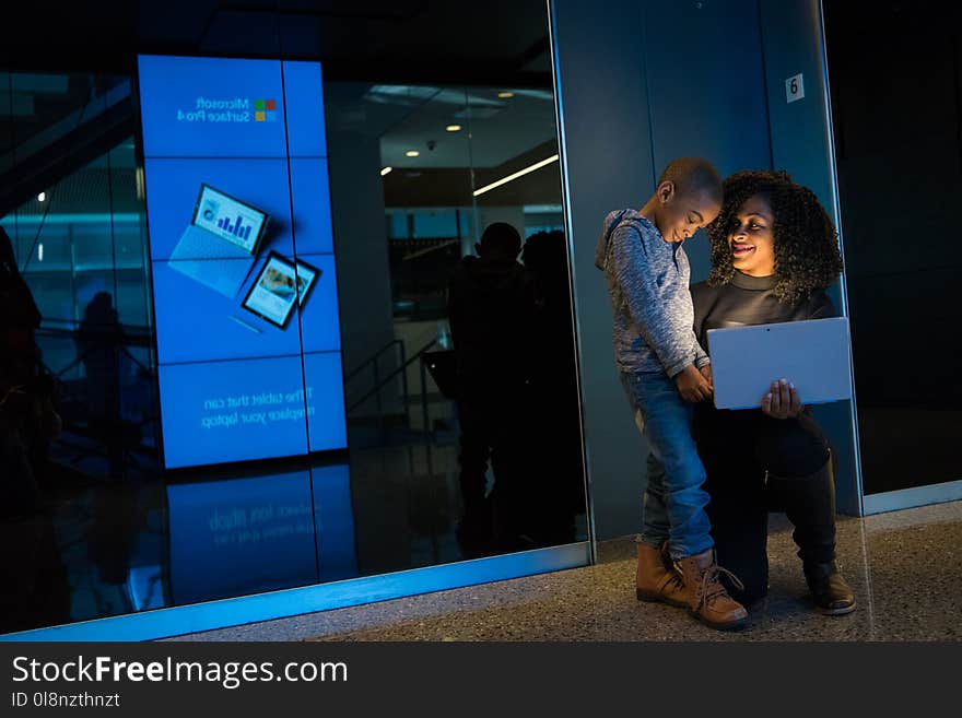 Boy in Gray Hoodie Standing Beside Woman Holding Laptop