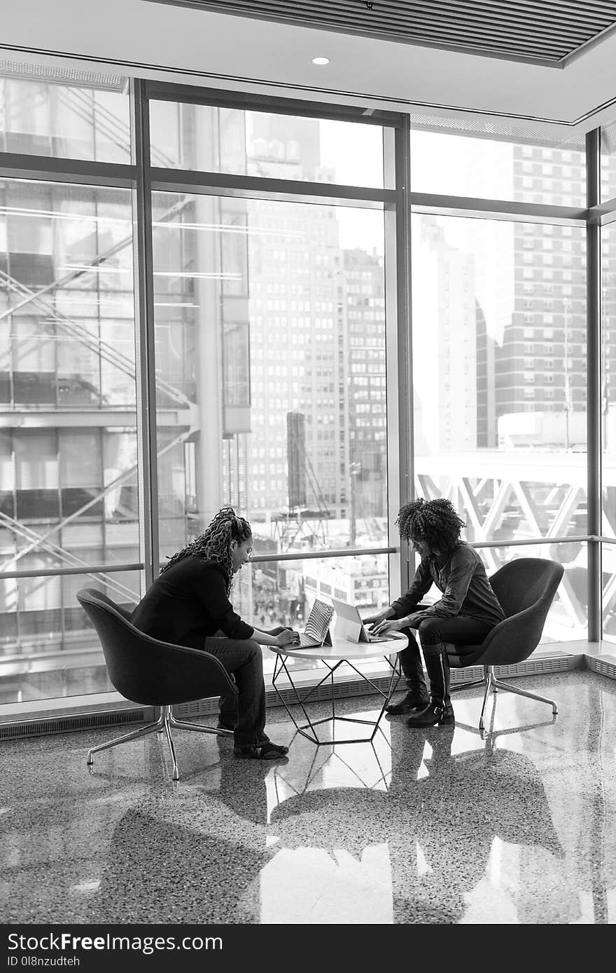 Grayscale Portrait of Two People Sitting on Chairs