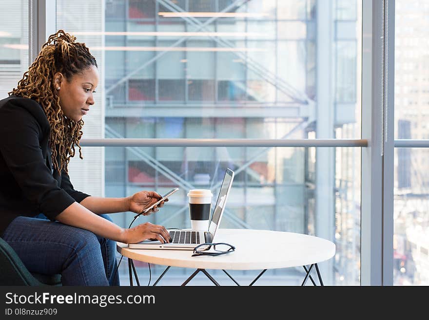 Woman Holding Smartphone Sitting in Front of Laptop on Table