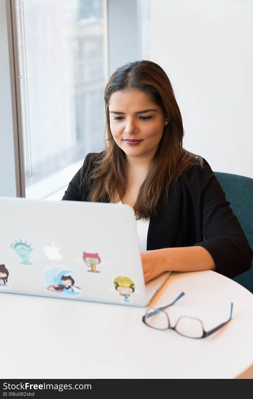 Woman Wearing Black Suit Jacket Using White Macbook With Stickers on White Wooden Table