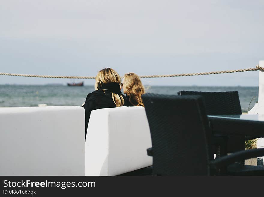 Two Women Sitting Near Body of Water