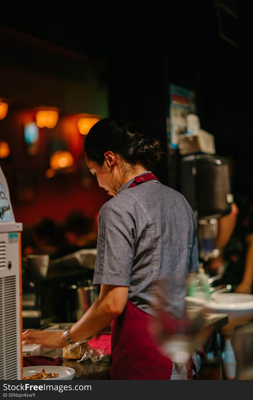 Person Wearing Red Apron Stands in Front of Table With Plate