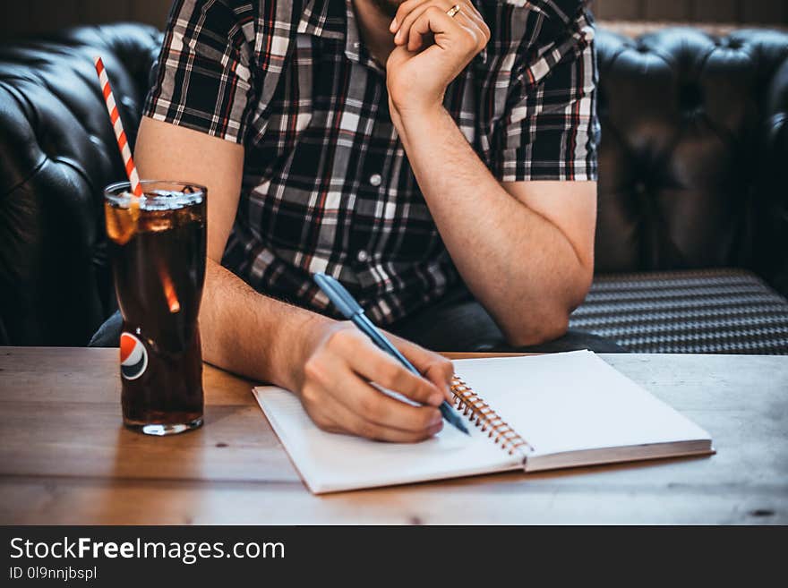 Man Holding Blue Pen Writing on White Notepad